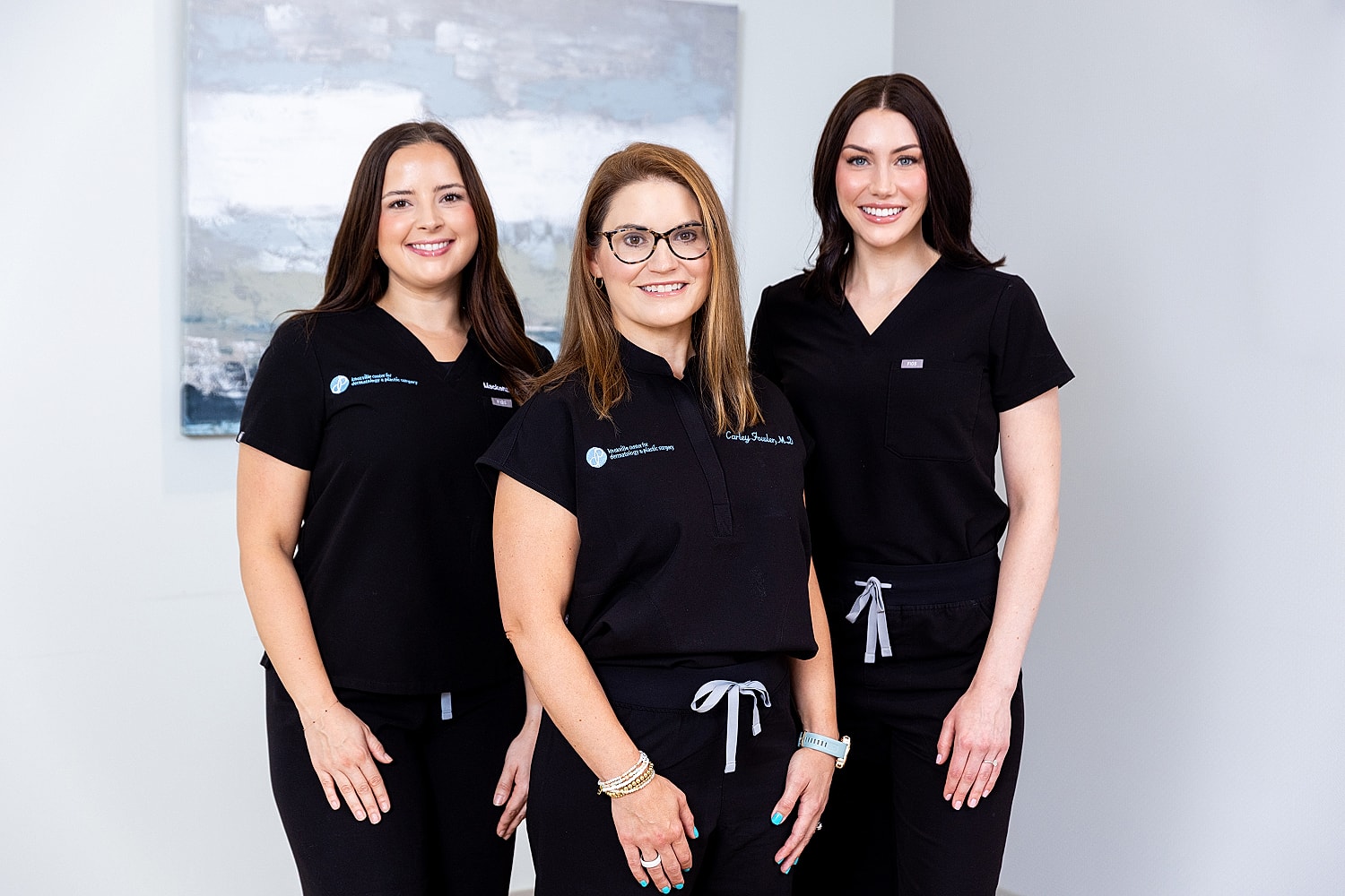 Three smiling professionals in black scrubs.