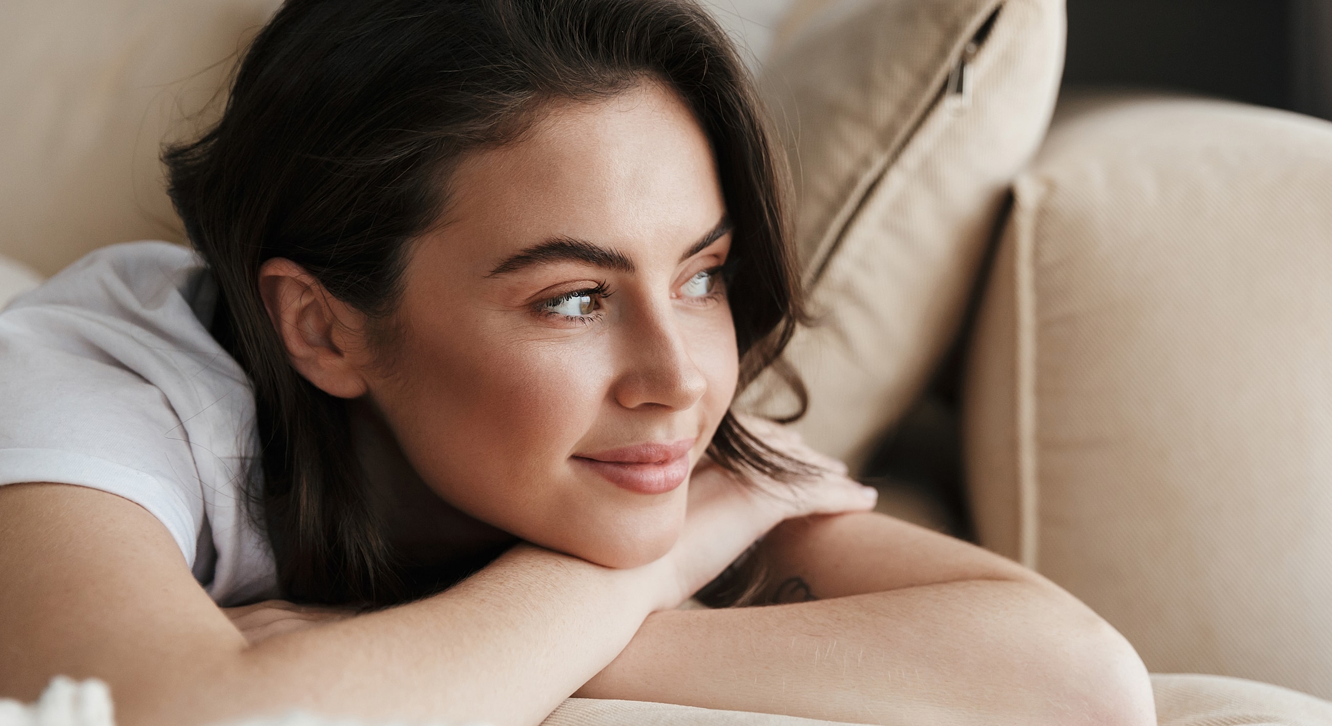 Woman relaxing on a couch, smiling thoughtfully.